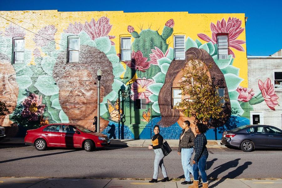 three students walk in front of a brightly colored mural